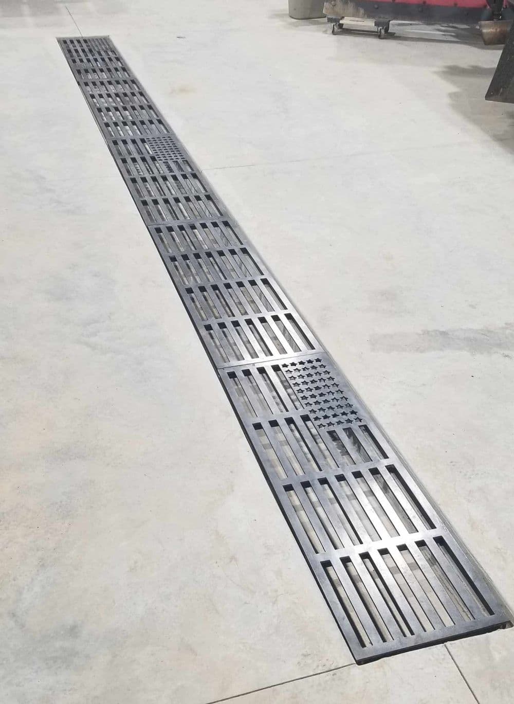 Metal grating with American flag design, laid out on a concrete floor in a workshop setting.