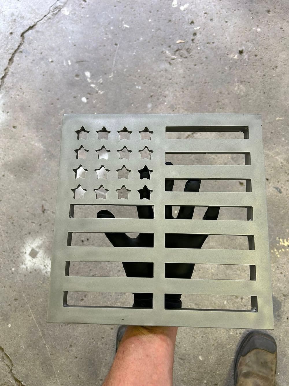 Metal American flag design held by a person wearing a black glove, on a concrete surface.