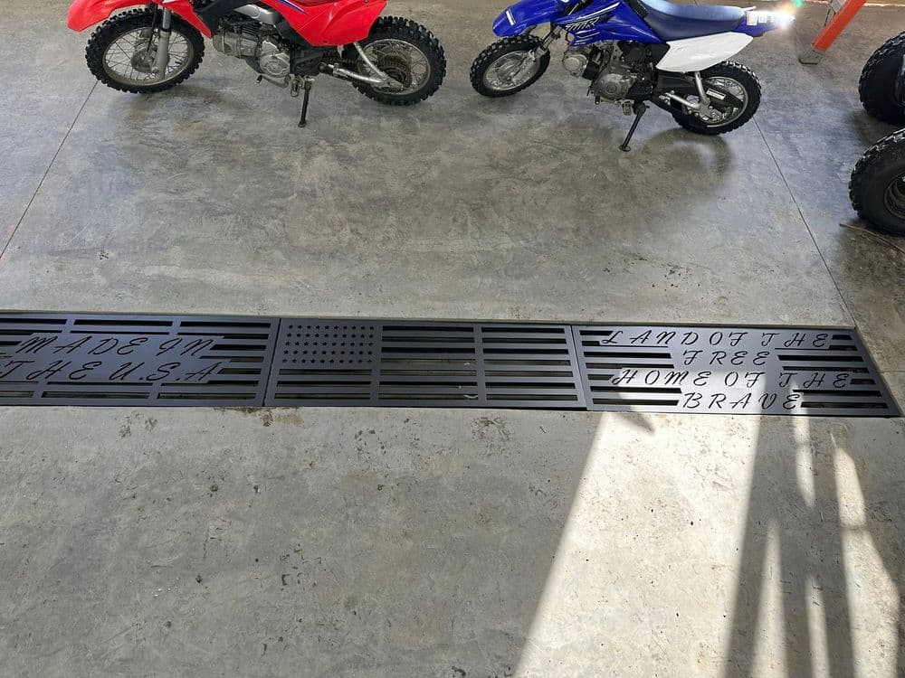 Metal grate with "Made in the USA" and "Land of the Free, Home of the Brave" designs.