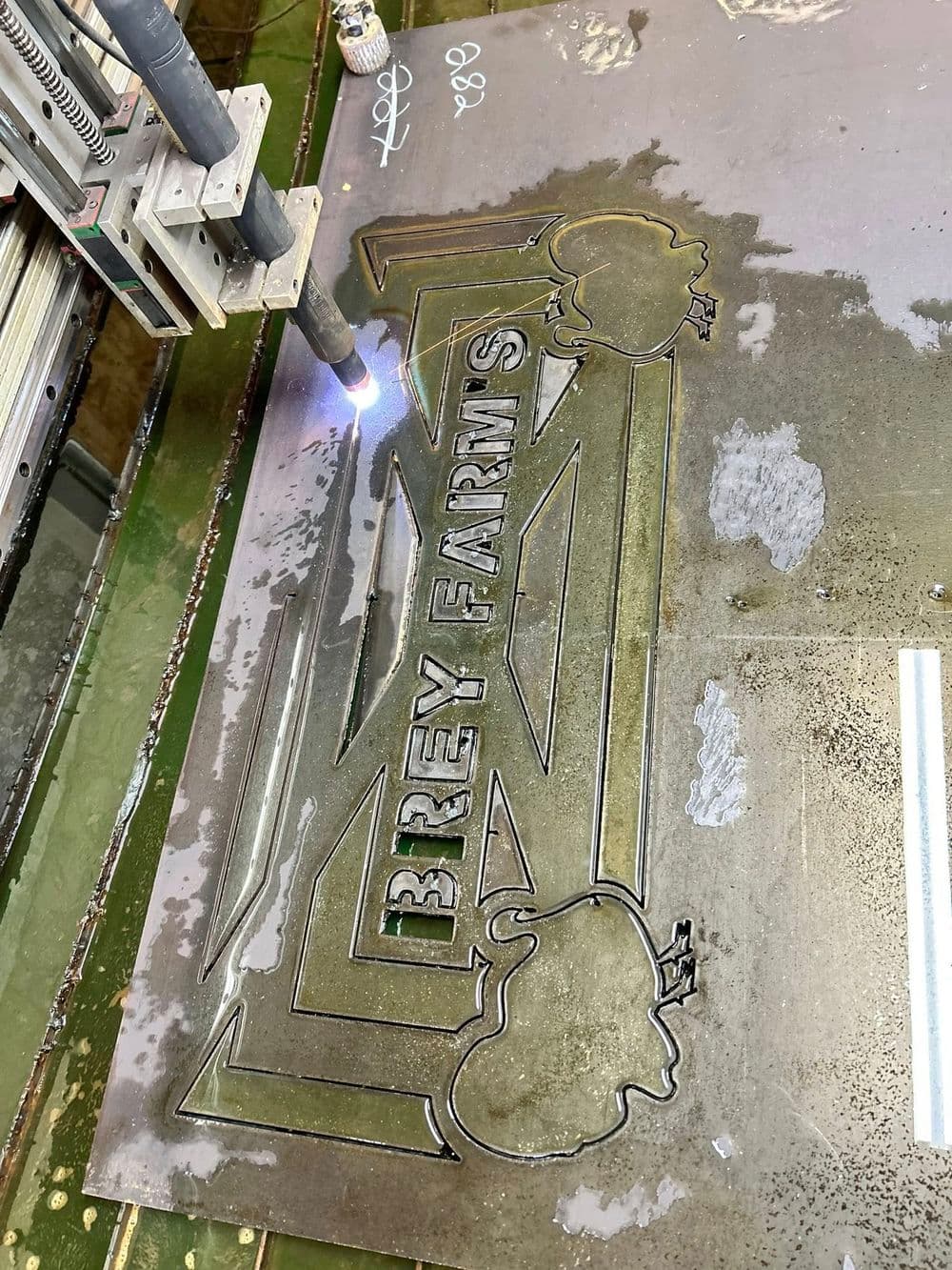 Brey Farms metal sign being cut with a plasma cutter in a workshop setting.