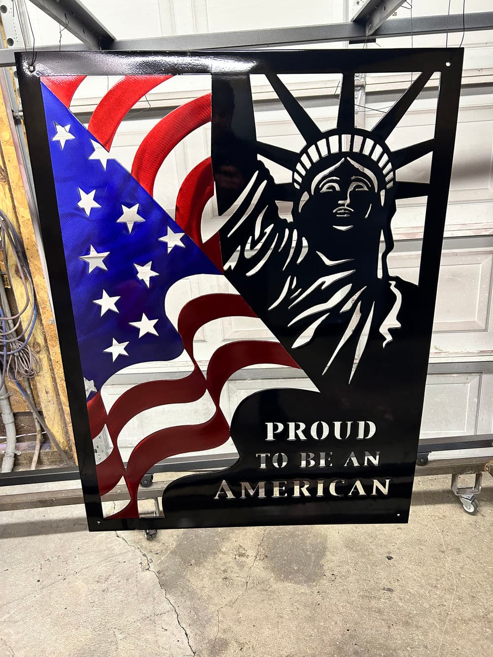 Metal art featuring the Statue of Liberty and American flag with the text "Proud to be an American."