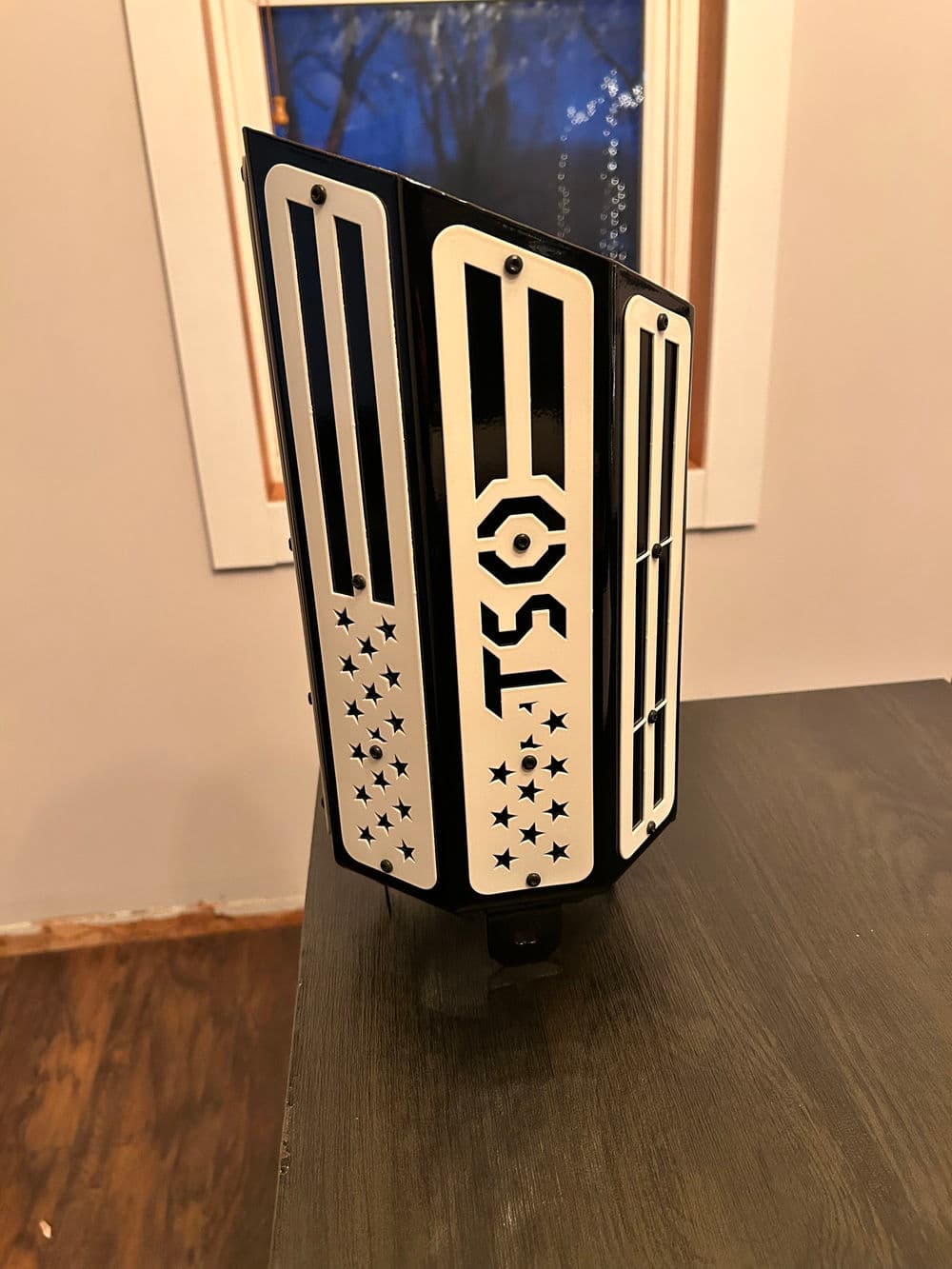 Black and white TSL guard with star design, displayed on a wooden table near a window.