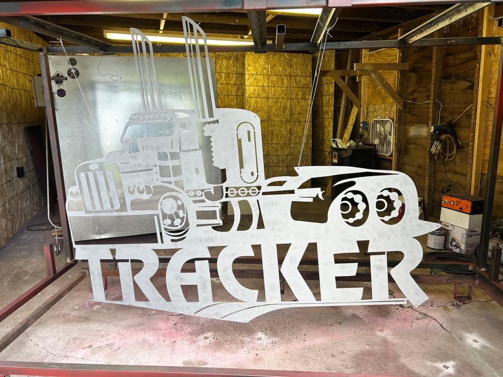 Metal cutout of a truck with the word "TRACKER" in bold letters on a workshop background.