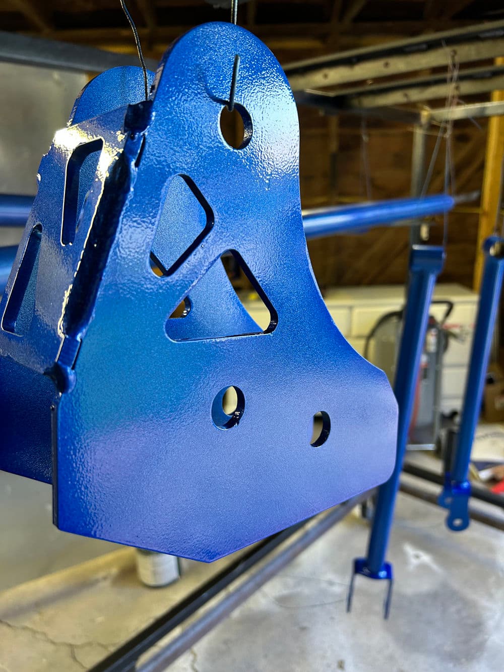 Blue metal bracket hanging in a workshop, featuring cutouts and a glossy finish.