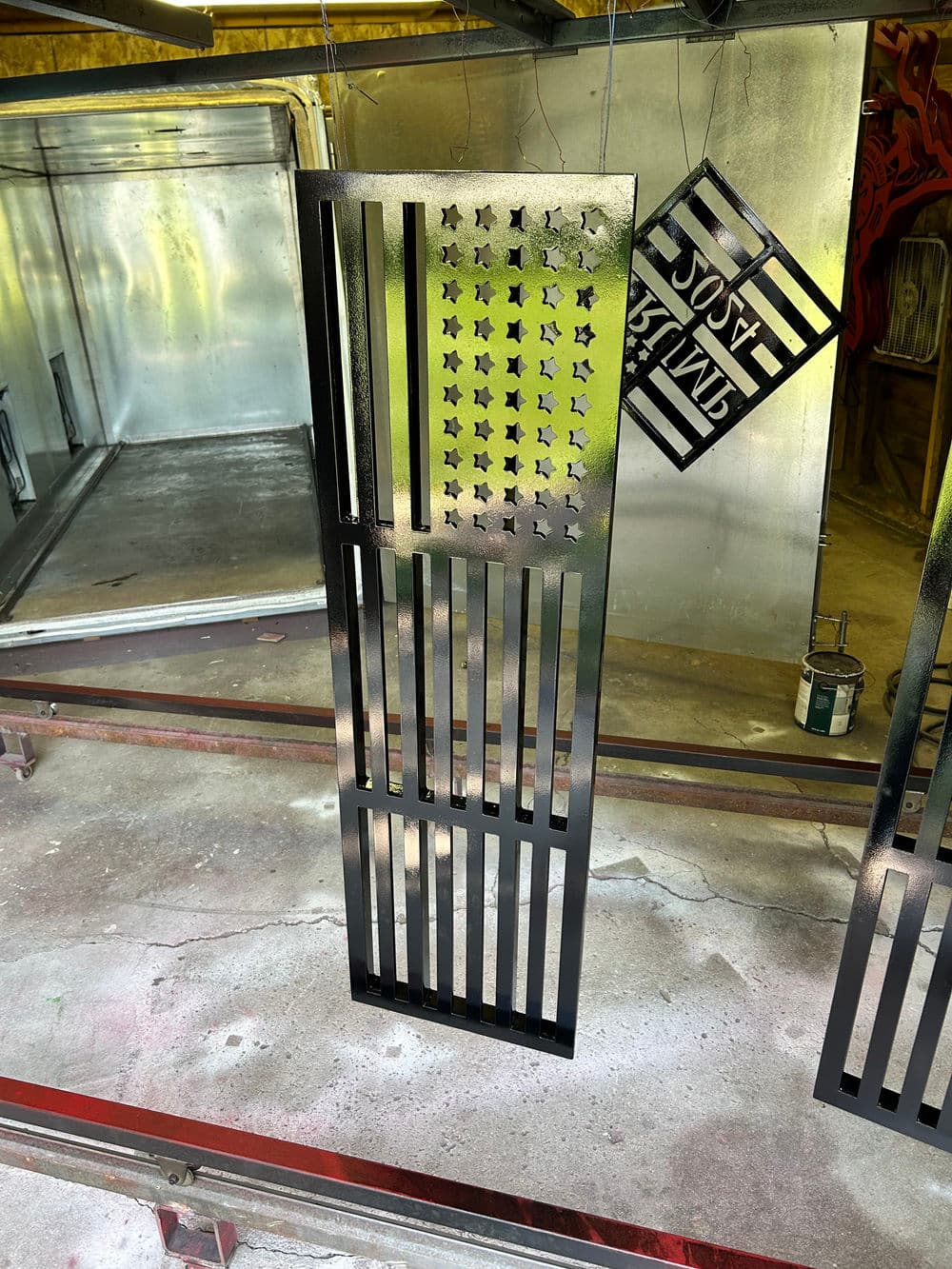 Black metal flag design with stars and stripes, displayed in an industrial workshop setting.