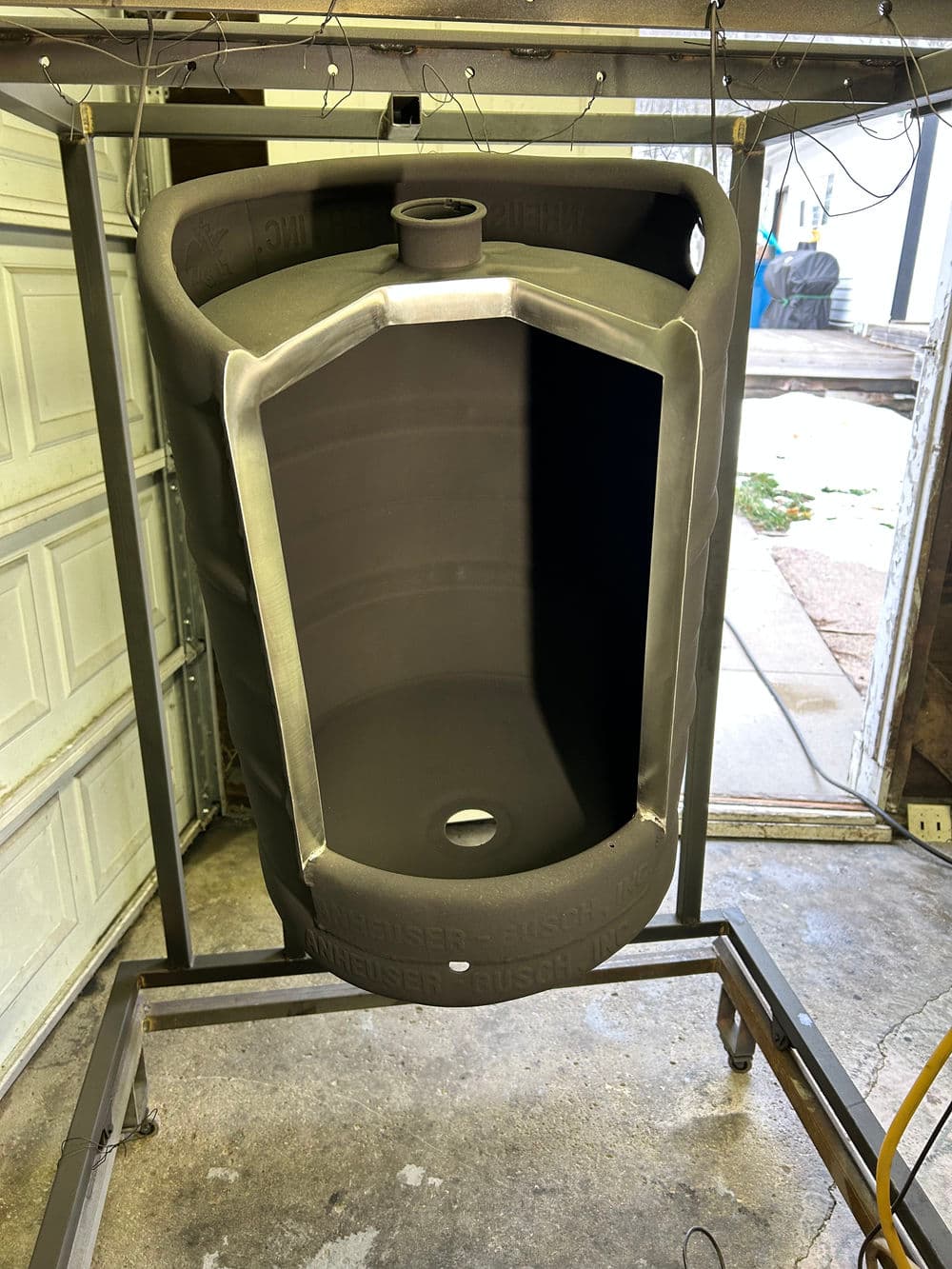 Empty black plastic keg on a metal stand in a garage setting, ready for use or modification.
