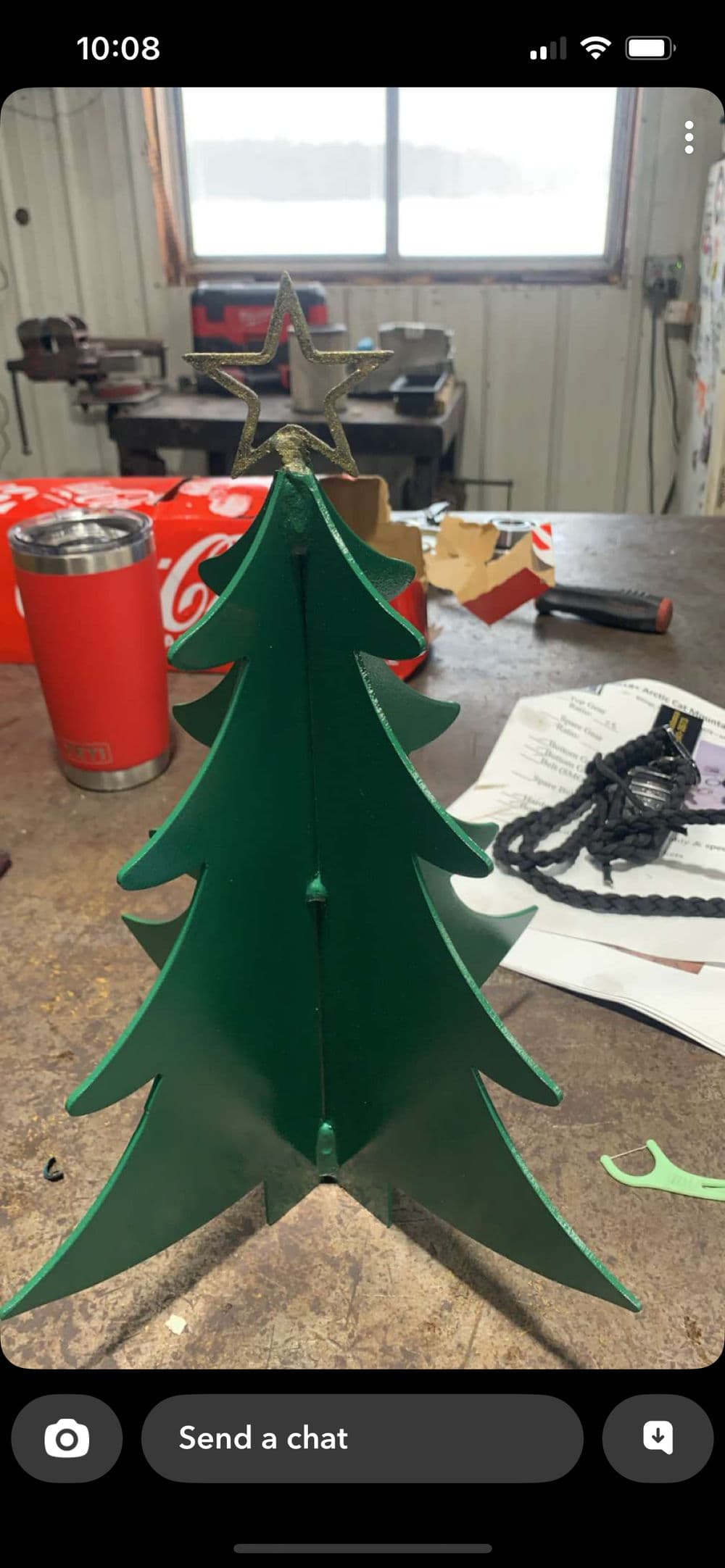 Green metal Christmas tree with star on top, set on a rustic workbench background.