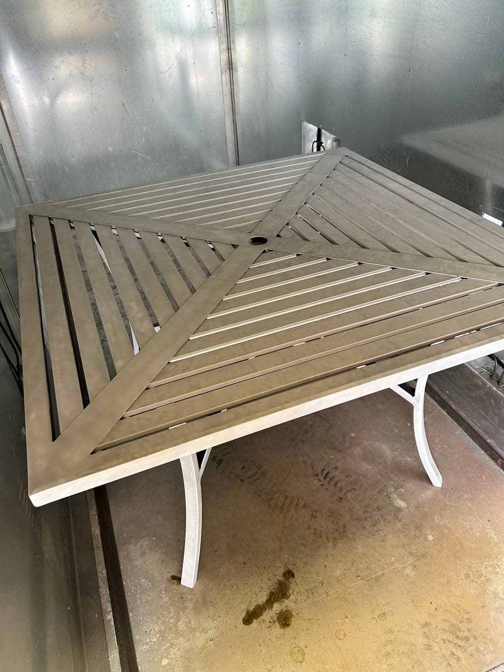 Metal outdoor dining table with a slatted top and decorative design, set indoors.