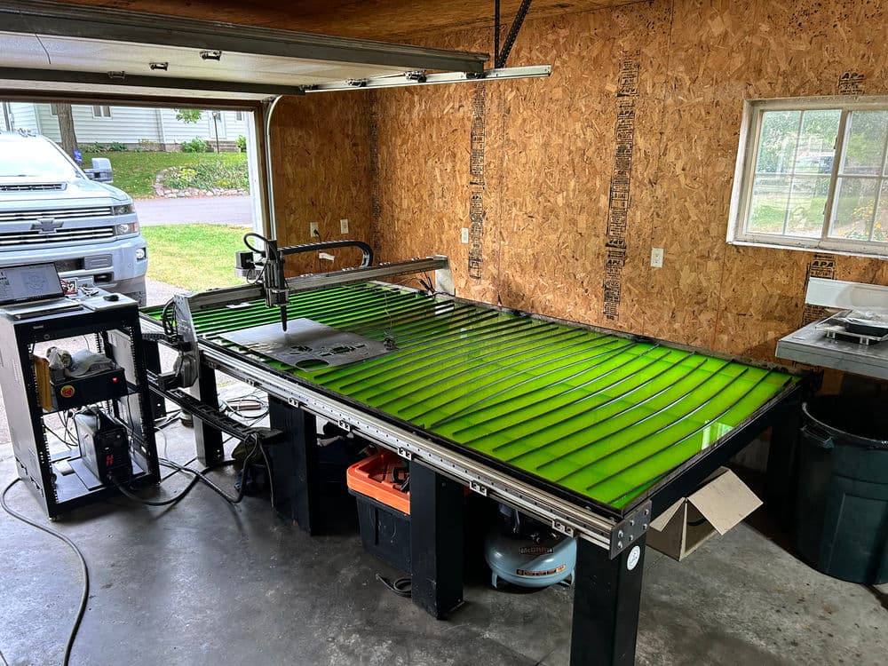 CNC plasma cutting table in a garage, featuring bright green cutting surface and tools.